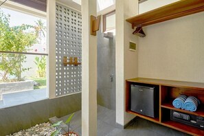 A bathroom with a shower, a small refrigerator, and towels on a shelf. - Ama-lurra Resort Gili Air (Gili Air)