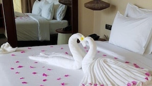 Habitación de hotel con una cama bien hecha, una lámpara colgante y vista al pasillo.