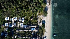 Vista aérea de un resort frente a la playa con varios edificios cuadrados, cada uno con piscina y rodeado de palmeras.