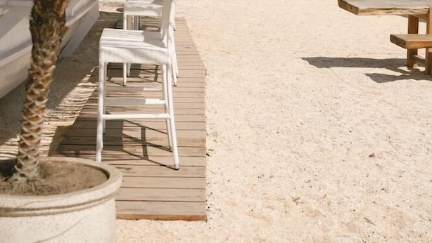 Un área de descanso frente a la playa con sillones blancos y sombrillas, una terraza de madera y vistas al mar.