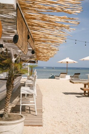 A beachside lounge area with white lounge chairs and umbrellas, a wooden deck, and a view of the sea. - Ama-lurra Resort Gili Air (Gili Air)