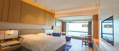 A modern hotel room with a large bed, bedside tables, a desk with a chair, and a view of the outdoors.