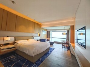 Una habitación de hotel moderna con una cama grande, mesitas de noche, un escritorio con una silla y vistas al exterior.
