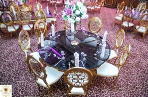 Una mesa redonda con superficie de vidrio rodeada de sillas ornamentales, sobre una alfombra estampada.