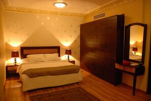 Une chambre d’hôtel comprenant un lit, des tables de chevet, une commode, un miroir et un mur orné d’un motif décoratif.