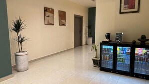 A hotel lobby with a tiled floor, a reception desk with a refrigerator stocked with beverages, and two framed artworks on the wall. - Sky Hotel Aqaba (Aqaba)