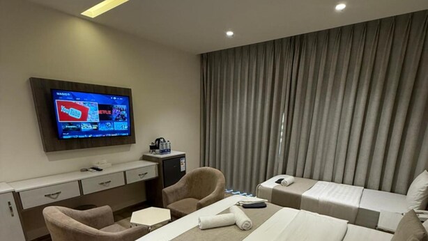 A hotel room with a large bed, two armchairs, a desk, a television, and a window with curtains. - Sky Hotel Aqaba (Aqaba)