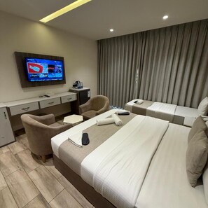 Une chambre d’hôtel avec un grand lit, deux fauteuils, un bureau, une télévision et une fenêtre avec des rideaux.