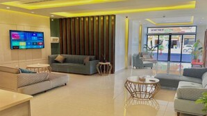 A modern hotel lobby with a sofa, two round tables, a flat-screen TV, and a view of the street outside. - Sky Hotel Aqaba (Aqaba)