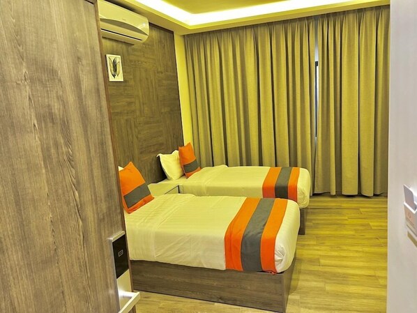 Quarto de hotel com duas camas, piso de madeira, uma janela grande com cortinas e um aparelho de ar condicionado.