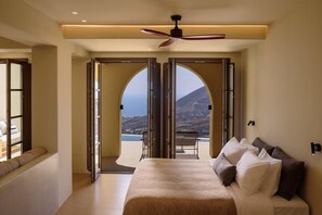 Une chambre à coucher avec un lit, un ventilateur de plafond et une porte ouverte donnant sur un balcon avec vue.