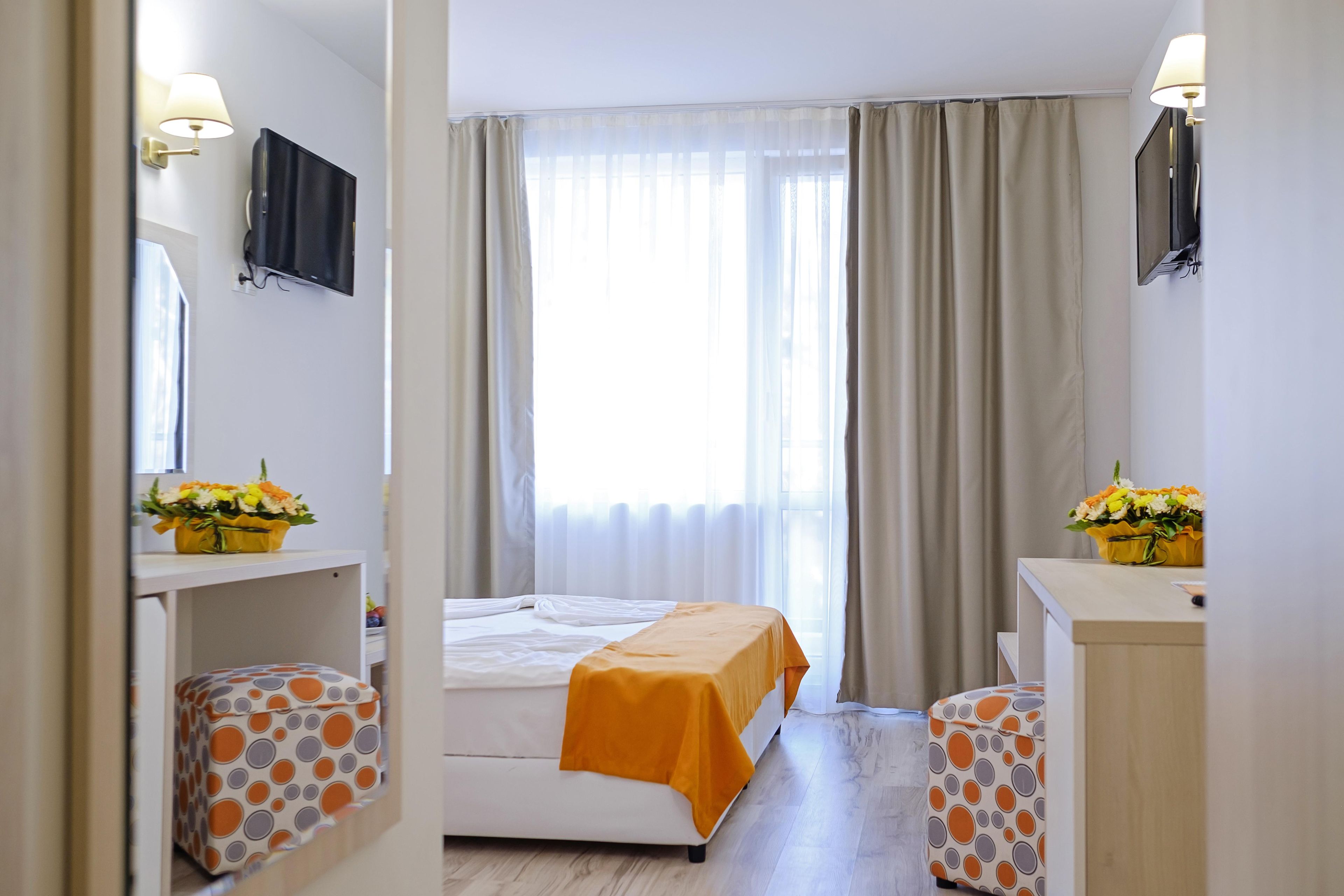 A hotel room with a bed, a television, a desk with a lamp, and a window with curtains.