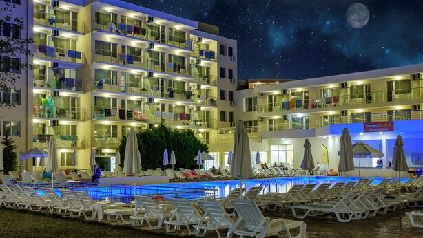 Ένα πολυώροφο ξενοδοχείο με πισίνα, ξαπλώστρες και ομπρέλες.