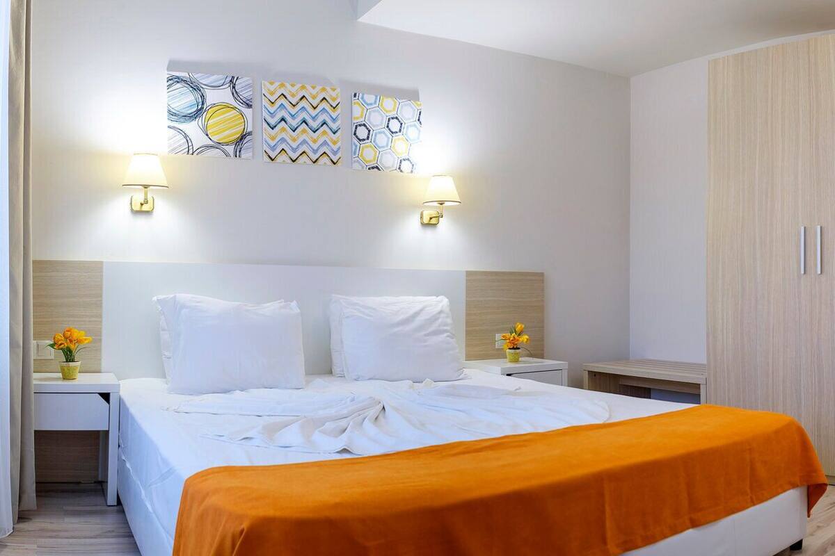 A hotel room with a bed, two bedside tables, a nightstand, a wardrobe, and wall art.