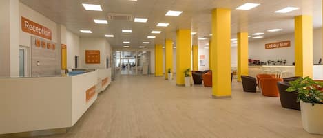 Un espace d’accueil comprenant un comptoir de réception, un bar dans le hall et des piliers jaunes.