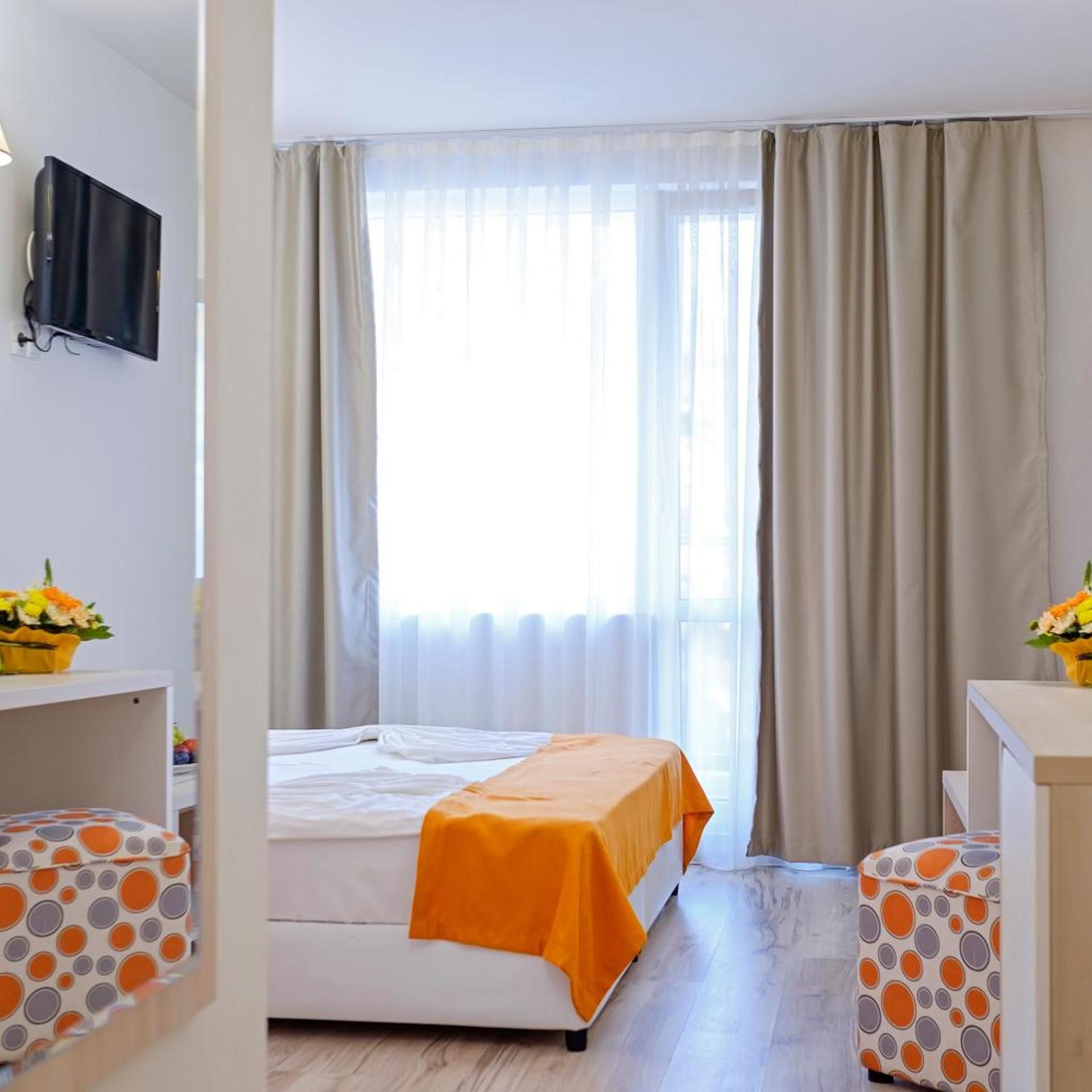 Habitación de hotel con cama, televisión, ventana con cortinas y escritorio con un arreglo floral.
