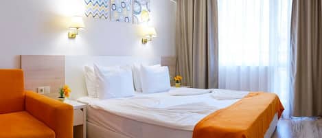 A hotel room with a bed, a nightstand, a lamp, a chair, and a window with curtains.