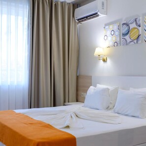 A hotel room with a bed, curtains, an air conditioning unit, a wall-mounted lamp, and artwork. - Hotel Garden Nevis (Nessebar)
