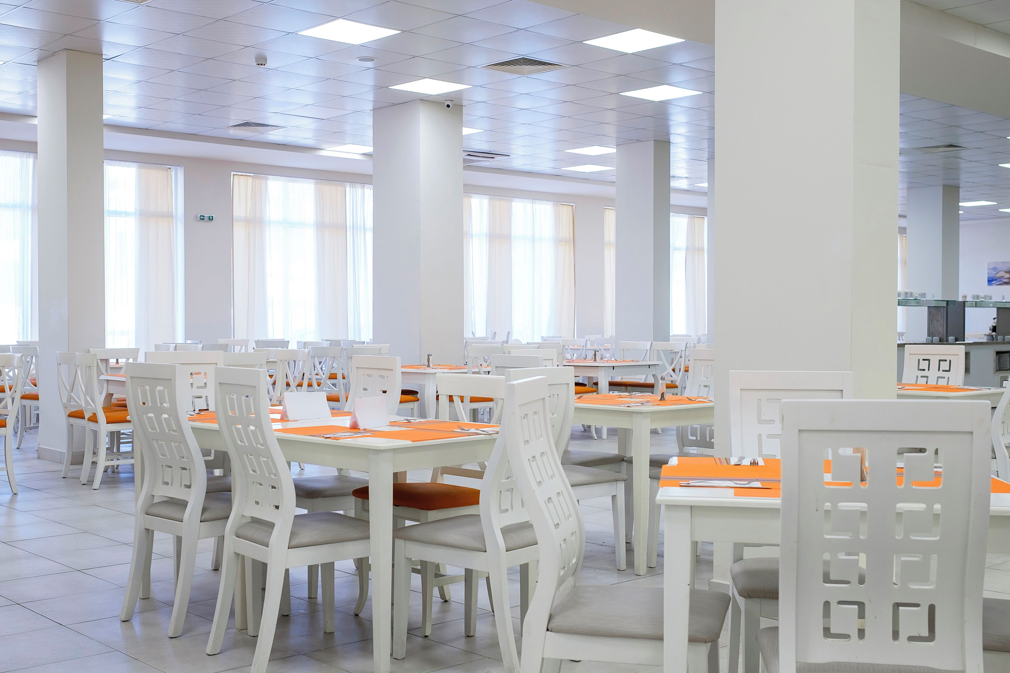 A spacious dining area with white tables and chairs, large windows, and a clean, modern design.