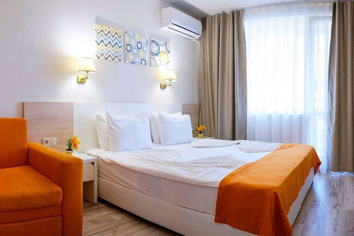 A hotel room with a bed, a nightstand, a lamp, a chair, and a window with curtains.