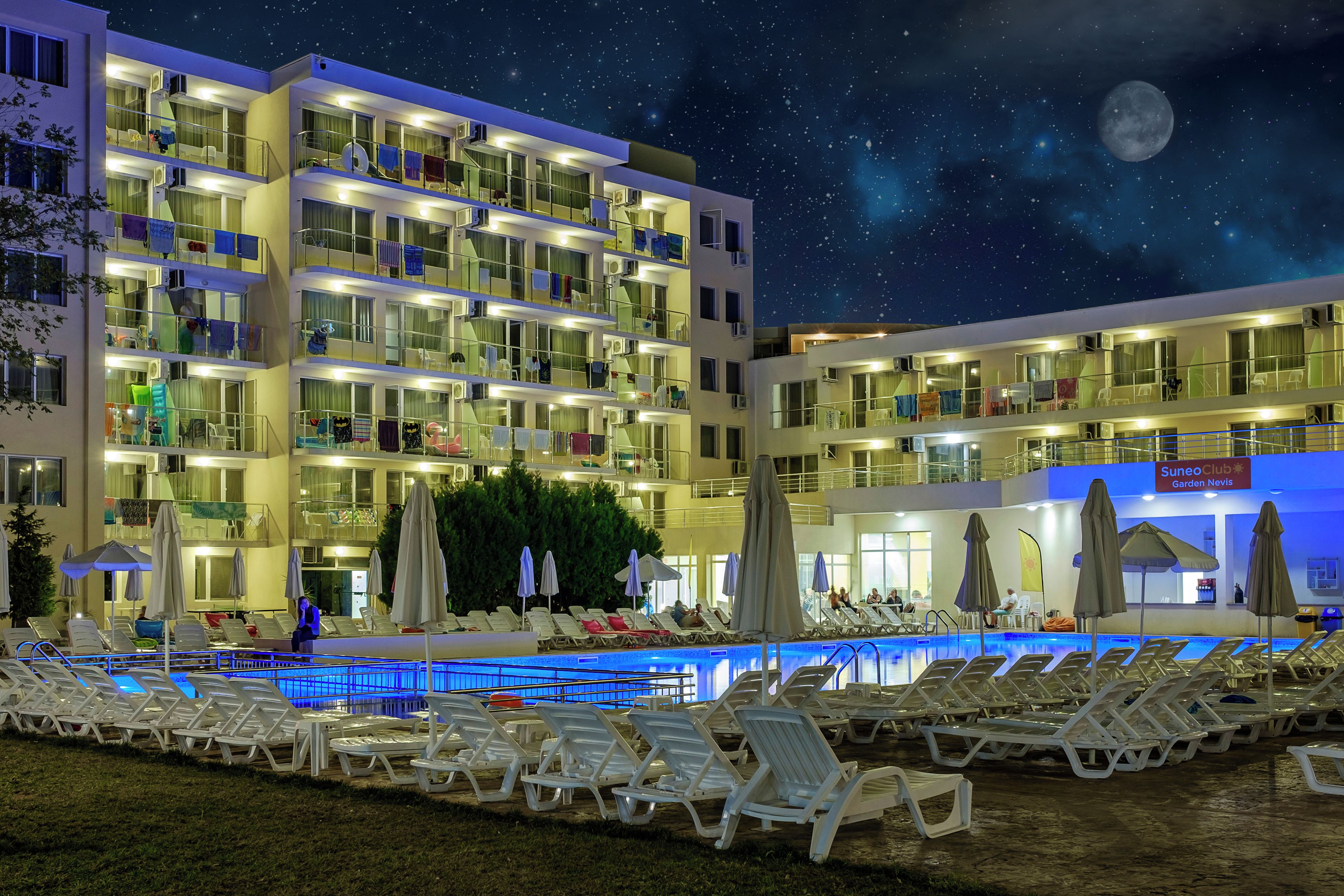 A multi-story hotel with a swimming pool, lounge chairs, and umbrellas.