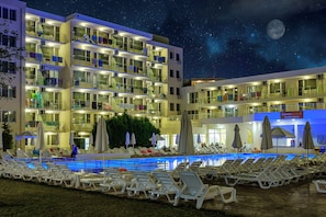 Un hotel de varios pisos con piscina, sillas de descanso y sombrillas.