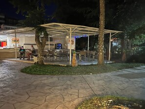 An outdoor seating area with tables and chairs, a covered structure, and a food counter. - Hotel Garden Nevis (Nessebar)