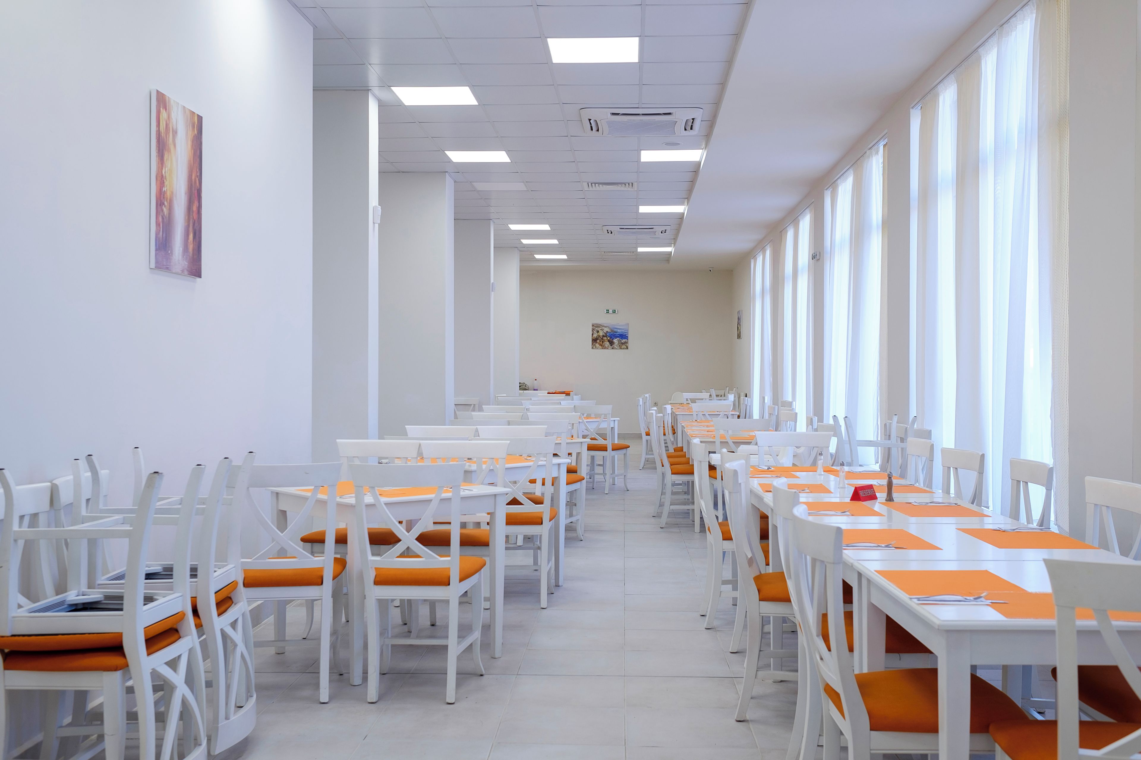 A long dining area with white tables and chairs, arranged in rows.