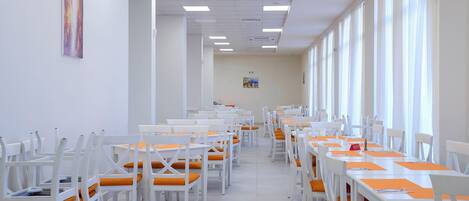 A long dining area with white tables and chairs, arranged in rows.