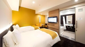 Ein Hotelzimmer mit zwei Betten, einem Fernseher, einem Schreibtisch und einem Badezimmer.