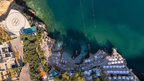 An aerial view of a coastal hotel with a swimming pool, beachside lounge areas, and a helipad. - Maritim Marina Bay Resort & Casino (Vlorë)