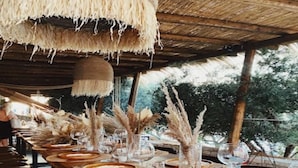 A long dining table set with plates, cutlery, and tall decorative vases, under a thatched roof structure. - Maritim Marina Bay Resort & Casino (Vlorë)