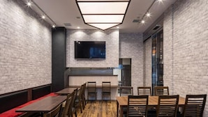 A modern dining area with brick walls, a flat-screen TV mounted above the counter, and wooden tables and chairs. - Apa Hotel (Tokyo)