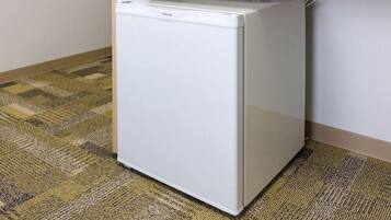 A white refrigerator in a corner of a room with a patterned carpet.