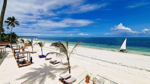 A beach with white sand, palm trees, lounge chairs, and a sailboat. - Dream of Zanzibar (Uroa)