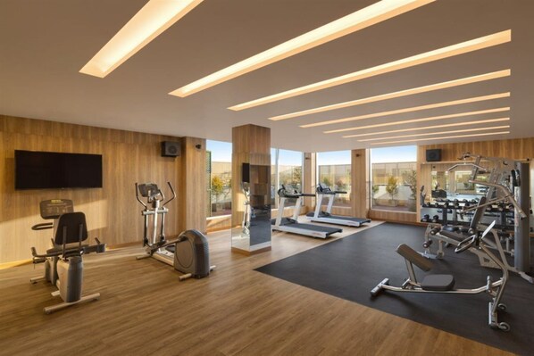 Un gimnasio moderno con equipo cardiovascular, máquinas de pesas y una pantalla de televisión grande.