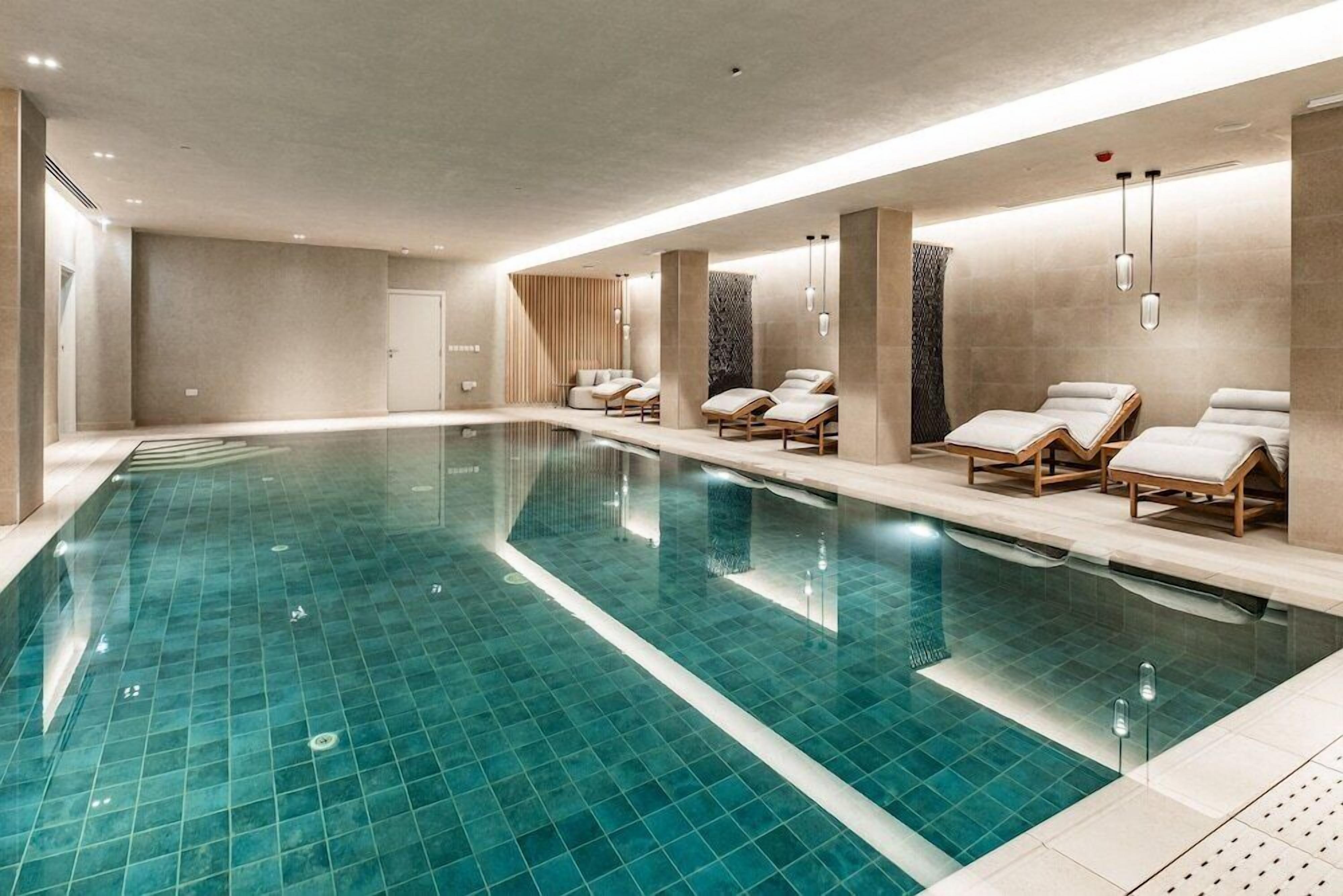 Una piscina interior moderna con sillones de descanso y zona de spa.