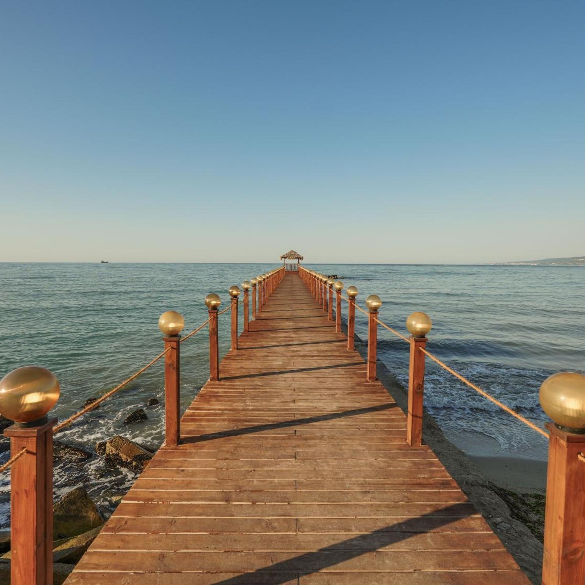 A wooden pier extending into calm waters with a clear sky above.