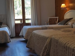 A room with two beds, a wooden floor, a window with curtains, a wall-mounted lamp, and a chair. - SNO Hotel Bielsa (Bielsa)