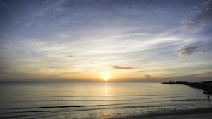 A beach with a sunset, calm water, and a distant shoreline. - Alexander Hotel Tegal (Tegal)