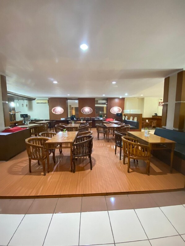 Un vaste espace dédié à la salle à manger, avec de nombreuses tables et chaises en bois, un bar central et un coin salon doté d’un canapé bleu.