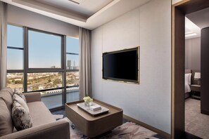 Een moderne hotelkamer met een groot raam, een flatscreen televisie aan de muur, een bank en een salontafel met een vaas en boek.