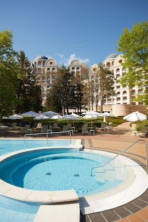 A swimming pool with lounge chairs and umbrellas, surrounded by trees and a building with domed architecture. - Alua Sunny Beach Resort & Spa (Nessebar)