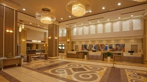 A hotel lobby with a reception desk, a coffee shop, and a large abstract art piece on the wall. - Alua Sunny Beach Resort & Spa (Nessebar)