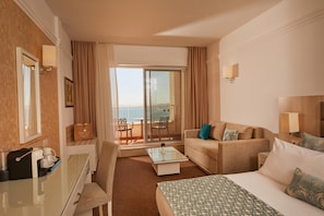 A hotel room with a bed, a sofa, a desk, a chair, a balcony with a view, and a sliding door. - Dreams Sunny Beach Resort SPA (Nessebar)