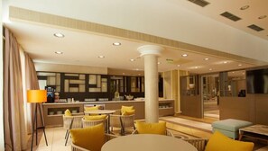 Un hall amplio con una zona de estar central, un mostrador de recepción y un espejo grande que refleja el espacio.