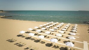 A beach with rows of sun loungers and umbrellas, a clear sky, and calm sea.