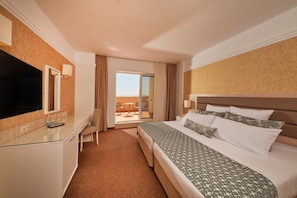 A hotel room with a bed, a desk, a TV, and a balcony with outdoor seating.