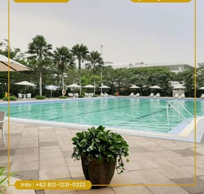 A swimming pool with lounge chairs and umbrellas, surrounded by palm trees and a building in the background. - Smart Dream Aeropolis AR2 Powered by Archipelago (Tangerang)