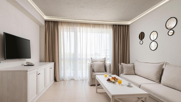 Une chambre d’hôtel moderne équipée d’un téléviseur à écran plat, d’une console blanche, d’un canapé beige et d’une table à manger avec des éléments pour le petit-déjeuner.